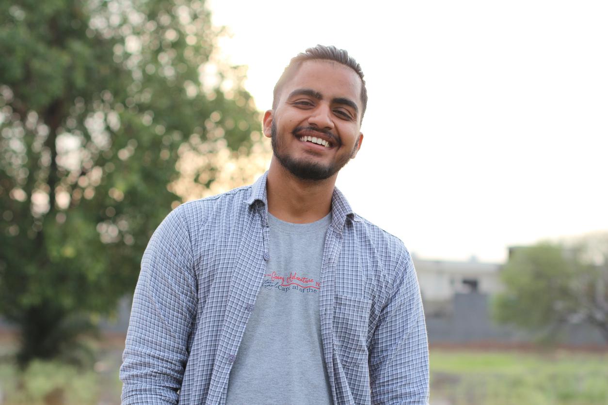 Young man smiles at the camera while standing outside at sunset.