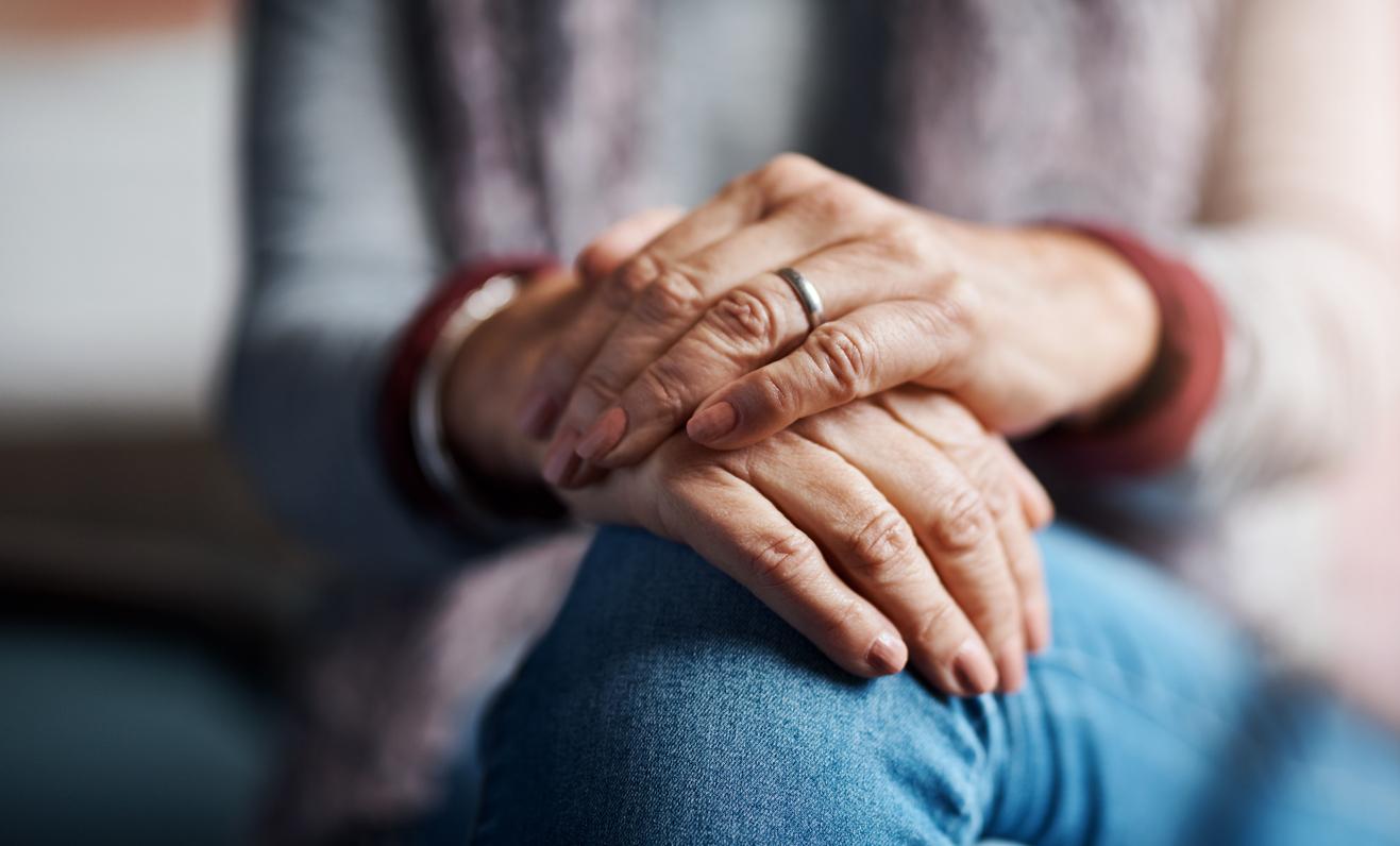 Hands of an older white woman folded on a lap.