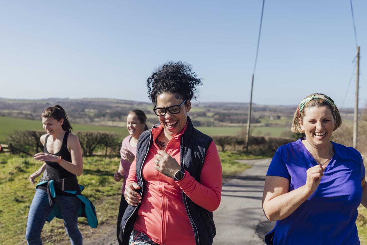Group of women running together and smiling outdoors on a sunny day.